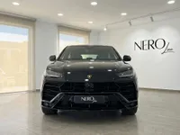 The black Lamborghini Urus SE is prominently displayed from the front in a bright showroom in Barcelona.
