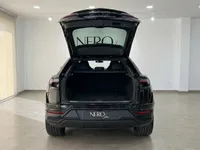 The rear view of a glossy black Lamborghini Urus SE in Barcelona, showcasing its spacious open trunk.