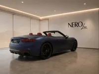 A matte dark blue Maserati GranCabrio convertible with its top down, showcasing its rear three-quarter view in a showroom in Lausanne.