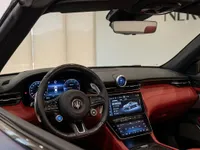 The luxurious interior of the 2024 Maserati GranCabrio in Lausanne, showcasing its red leather dashboard, digital displays, and carbon fiber steering wheel.