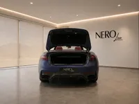 The rear view of a matte dark blue Maserati GranCabrio with its trunk open, parked in a showroom in Lausanne.