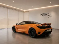 The striking orange McLaren 750S is showcased from a rear three-quarter angle in a modern showroom in Lausanne.