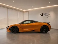 The vibrant orange McLaren 750S is showcased in a side profile view, parked in a modern showroom in Lausanne.