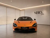 The Gloss Orange McLaren 750S supercar is prominently displayed in a modern showroom with the NEROline logo on the wall in Lausanne.