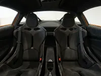 The luxurious interior of the McLaren 750S in Lausanne, featuring black Alcantara sports seats with orange stitching and carbon fiber accents.