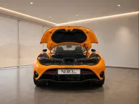 The Gloss Orange McLaren 750S is showcased from the rear with its engine bay open, parked in a modern showroom in Lausanne.