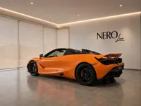 The orange McLaren 750S Spider is parked with its top down, showcasing its sleek rear three-quarter view in a modern showroom in Zurich.