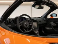 The image shows the luxurious black interior and dashboard of the orange McLaren 750S Spider in Zurich, viewed from the passenger side.