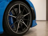 The Gloss Bright Blue McLaren 765LT Spider's front wheel, showcasing its black multi-spoke rim and blue brake caliper in Lausanne.