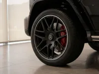 Close-up of the Mercedes-AMG G 63's black multi-spoke wheel with red brake calipers and glossy obsidian black body in Zurich.