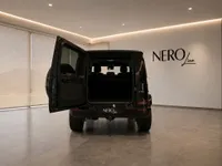 The rear view of a black Mercedes-AMG G 63 with its trunk open, parked in a modern showroom in Zurich.
