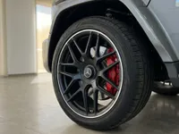 The Mercedes-Benz G63 AMG in gloss Arabian Grey showcases its black multi-spoke wheel and vibrant red brake caliper in Ibiza.