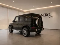 A black Mercedes-Benz G63 AMG is parked in a showroom, viewed from the rear three-quarter angle in Lausanne.