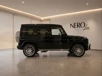 The black Mercedes-Benz G63 AMG is showcased in a modern showroom in Lausanne, viewed from its elegant side profile.