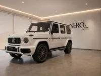 The white Mercedes-Benz G63 AMG is showcased from a front three-quarter angle inside a modern showroom in Lausanne.
