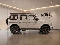A white Mercedes-Benz G63 AMG is showcased in a modern showroom with a large window revealing mountains in Lausanne.