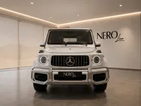 The white Mercedes-Benz G63 AMG 2021 is prominently displayed from the front in a showroom in Lausanne.