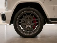 The front wheel of a white Mercedes-Benz G63 AMG in Lausanne, showcasing its dark grey rim and red brake caliper.