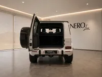 The white Mercedes-Benz G63 AMG is shown from the rear with its boot open, revealing the spacious cargo area and spare tire in Lausanne.