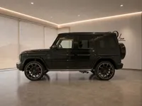 The gloss black Mercedes-Benz G63 Brabus is showcased in a modern showroom, revealing its powerful side profile in Lausanne.