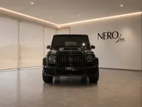 The black Mercedes-Benz G63 Brabus (G-Class) is prominently displayed from the front in a modern showroom in Lausanne.