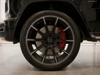 The front wheel of a gloss black Mercedes-Benz G63 Brabus in Lausanne, featuring a black Brabus rim and red brake caliper.