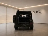 The rear view of a black Mercedes-Benz G63 Brabus with its trunk open, showcasing the spacious interior in a Lausanne showroom.