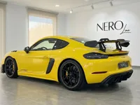 بورشه 718 كايمان GT4 RS الصفراء، منظر خلفي ثلاثي الأرباع، تبرز جناحها الكبير وعجلاتها السوداء في صالة عرض أليكانتي.