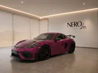 The gloss Ruby Star Neo Porsche 718 Cayman GT4 RS is showcased from a front three-quarter view in a modern showroom in Zurich.