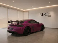 The striking gloss Ruby Star Neo Porsche 718 Cayman GT4 RS is showcased from a rear three-quarter view in a modern Zurich showroom.