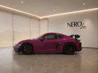 The 2023 Porsche 718 Cayman GT4 RS in gloss Ruby Star Neo, viewed from the side in a modern Zurich showroom.