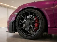 Close-up of the 2023 Porsche 718 Cayman GT4 RS in gloss Ruby Star Neo, highlighting its black wheel and red brake caliper in Zurich.