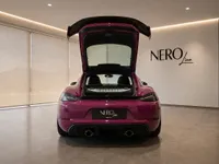 Rear view of the gloss Ruby Star Neo Porsche 718 Cayman GT4 RS with its open trunk, revealing the engine bay and interior in Zurich.