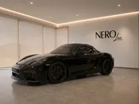 A gloss black 2021 Porsche 718 Spyder convertible is presented from a front three-quarter view in a modern Zurich showroom.