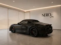 The gloss black Porsche 718 Spyder is showcased from a rear three-quarter view in a modern NEROline showroom in Zurich.