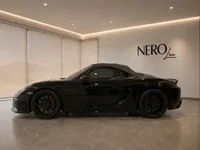 A sleek black Porsche 718 Spyder is showcased in a modern showroom with the NeroLine logo on the wall in Zurich.
