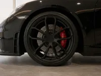The front wheel of the black Porsche 718 Spyder in Zurich, showcasing its matte black rim and red brake caliper.