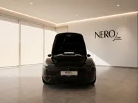 The black Porsche 718 Spyder is shown from the rear with its front trunk open, parked in a modern Zurich showroom.
