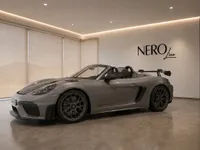 The grey Porsche 718 Spyder RS convertible is showcased from a side profile with its top down in a modern Zurich showroom.