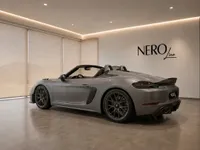 The grey Porsche 718 Spyder RS is showcased from a rear three-quarter angle in a modern NeroLine showroom in Zurich.