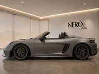 The grey Porsche 718 Spyder RS convertible is parked sideways in a modern showroom in Zurich, roof down, showcasing its sleek profile.