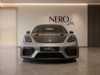 A grey 2024 Porsche 718 Spyder RS is parked head-on in a modern showroom in Zurich, featuring a carbon fiber hood.