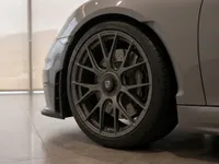 A close-up view of the grey Porsche 718 Spyder RS's front wheel, tire, and fender, showcasing its intricate rim design in Zurich.