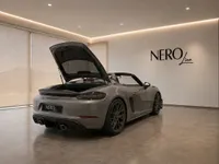 The grey Porsche 718 Spyder RS is shown from the rear-three-quarter view with its trunk open in a modern Zurich showroom.
