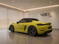 The vibrant yellow Porsche 718 Spyder RS with its black soft top is showcased in a modern Nero Line showroom in Zurich.