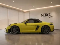 Yellow Porsche 718 Spyder RS convertible, with its black soft top up, parked in a modern showroom in Zurich.