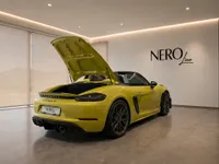 The yellow Porsche 718 Spyder RS is shown from the rear three-quarter angle with its engine cover open in a Zurich showroom.