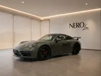 The gloss Aventurine Green Metallic Porsche 911 Carrera 4 GTS Aerokit is showcased from a front three-quarter view in a modern Zurich showroom.