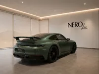 The gloss Aventurine Green Metallic Porsche 911 Carrera 4 GTS Aerokit is showcased from a rear three-quarter view in a modern Zurich showroom.