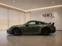 The Porsche 911 Carrera 4 GTS in gloss Aventurine Green Metallic, displayed in a side profile view inside a showroom in Zurich.